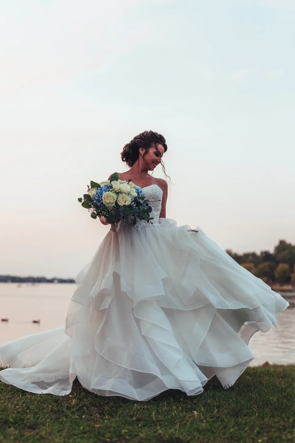 Braut im ausladenden Brautkleid mit Strauß am Seeufer