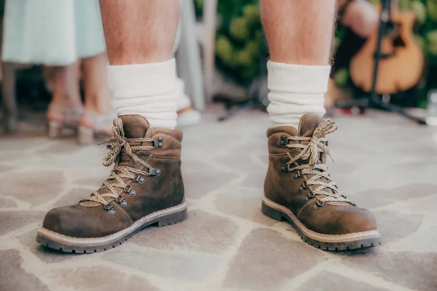 Bergschuhe mit weißen Wollsocken auf Steinplatten, dahinter unscharf eine Gitarre und Gäste
