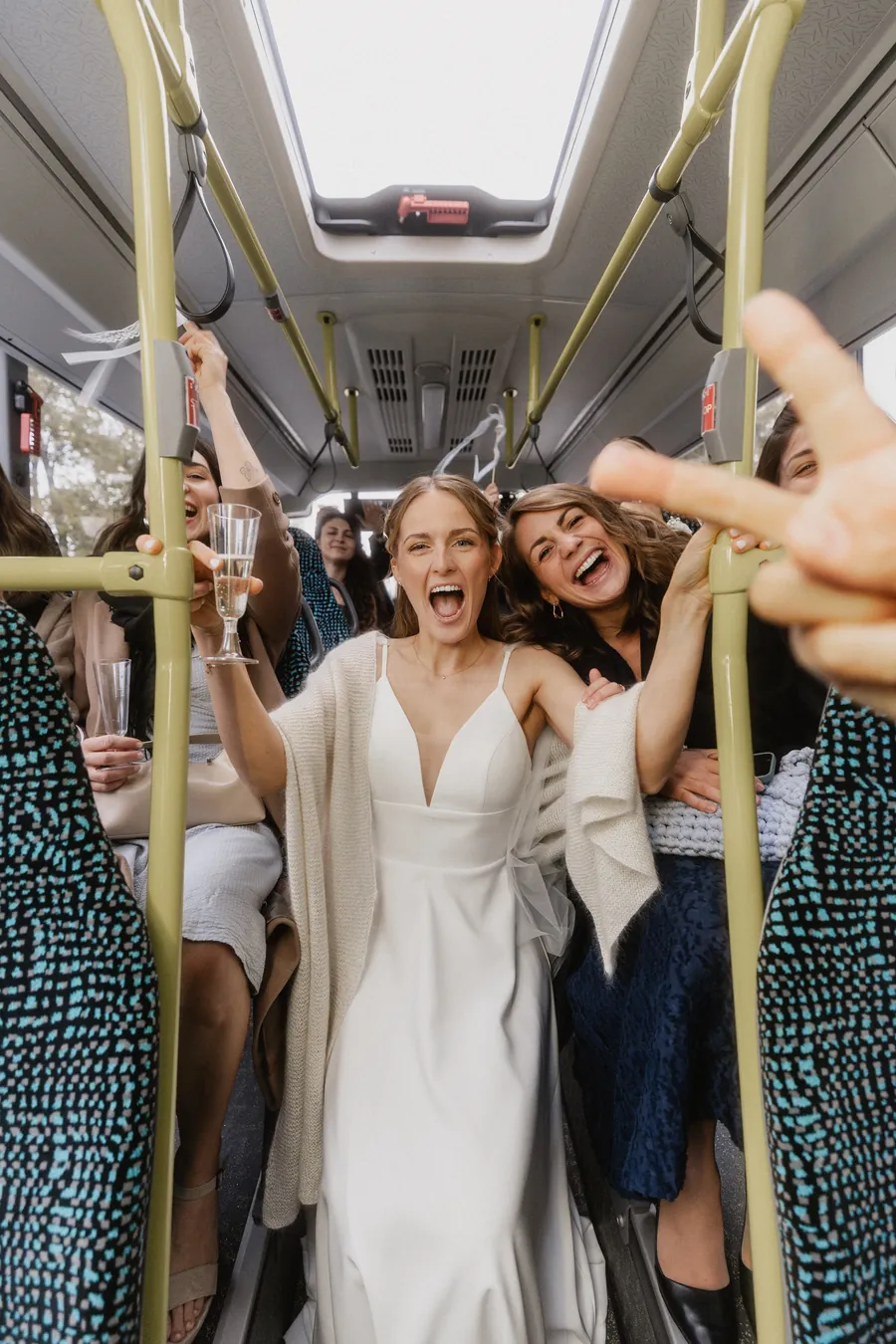 Braut und Freundinnen feiern im Bus und jubeln mit Sektgläsern