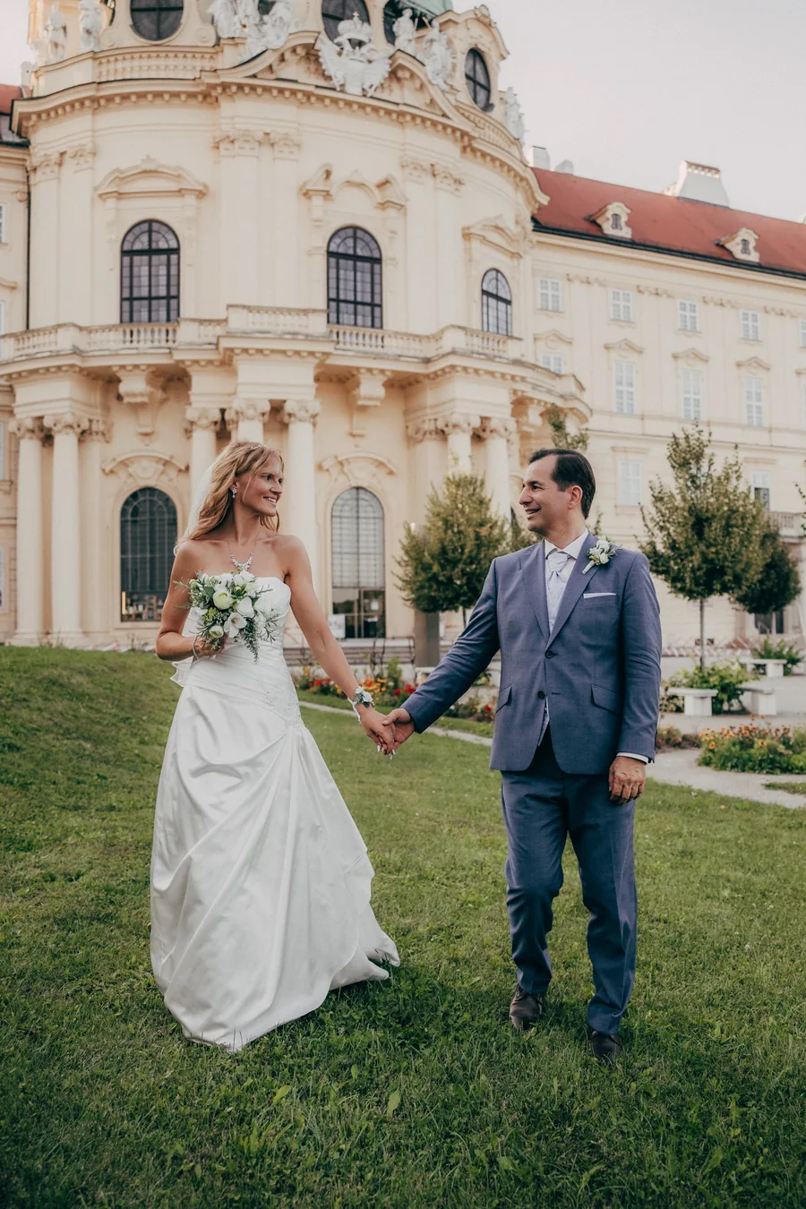 Brautpaar geht Hand in Hand über den Rasen vor einem barocken Schloss