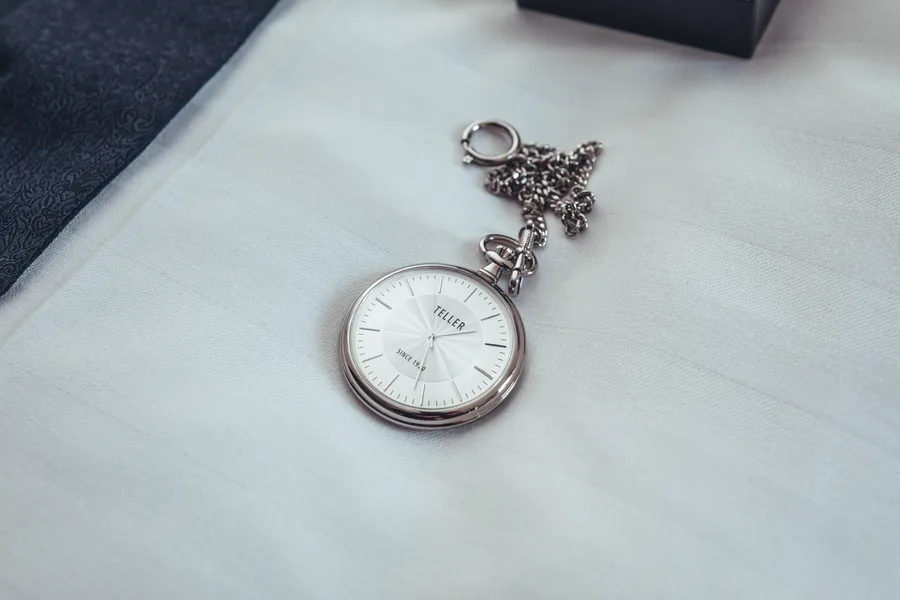 Silberne Taschenuhr mit Kette auf weißem Stoff