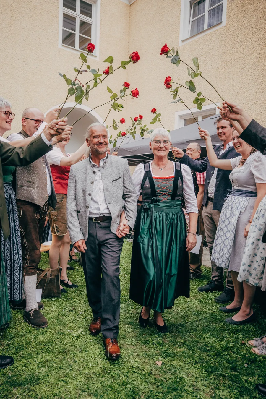 Brautpaar geht Hand in Hand durch ein Spalier aus Gästen mit erhobenen roten Rosen